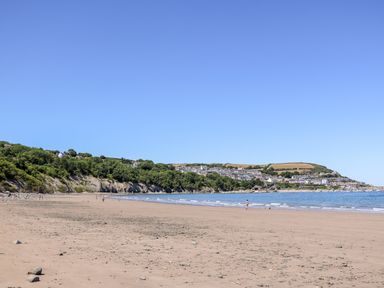 A beach with sand and scattered rocks near a coastal town with houses and green hills at Valley View Hideaway in Ffostrasol