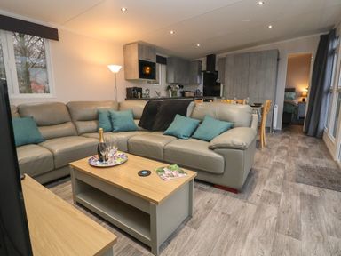 A living room with a gray sectional sofa blue pillows a wooden coffee table and an open kitchen at Holmside Audley Brow near Market Drayton