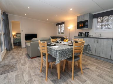 A dining area with a table set for four and a kitchen with grey cabinets and appliances at Holmside in Audley Brow near Market Drayton