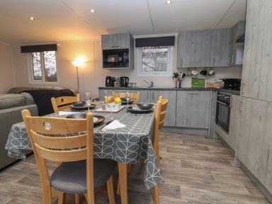 A kitchen and dining area with wooden chairs and a table with a patterned tablecloth at Holmside in Audley Brow near Market Drayton