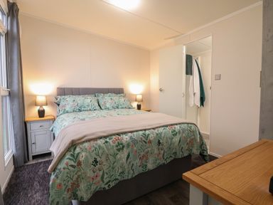 A bedroom with a bed with floral bedding two bedside tables with lamps and an open door showing towels at Holmside in Audley Brow near Market Drayton