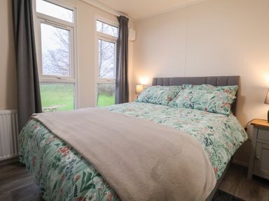 A bedroom with a bed covered in floral bedding two windows with grey curtains and bedside tables with lamps at Holmside Audley Brow near Market Drayton
