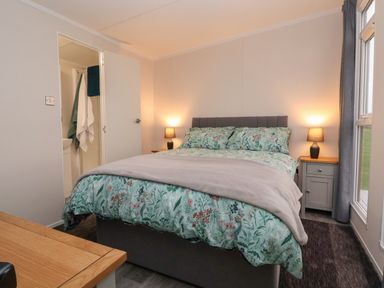 A bedroom with a double bed with floral bedding two bedside tables with lamps a window and a door leading to a bathroom at Holmside Audley Brow near Market Drayton