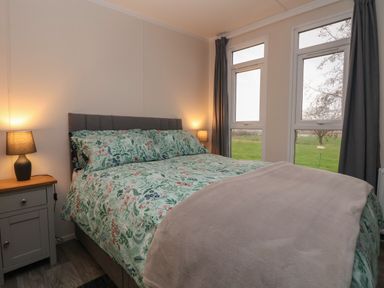 A bedroom with a double bed with floral bedding two lamps on bedside tables and large windows with curtains at Holmside in Audley Brow near Market Drayton