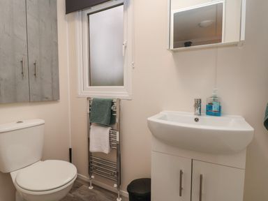 A bathroom with a toilet a sink with cabinet a mirror a towel rack with towels and a window at Holmside in Audley Brow near Market Drayton