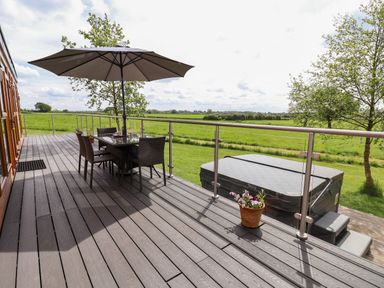An outdoor deck with a table and chairs under an umbrella and a hot tub overlooking green fields at Holmside in Audley Brow near Market Drayton