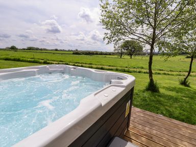 An outdoor hot tub on a wooden deck overlooking a grassy field with trees at Holmside in Audley Brow near Market Drayton