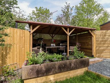 A wooden gazebo with seating and a barbecue grill behind a flower bed at Holmside Audley Brow near Market Drayton