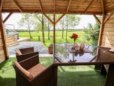 A covered outdoor seating area with a glass table and wicker chairs overlooking a grassy field at Holmside Audley Brow near Market Drayton