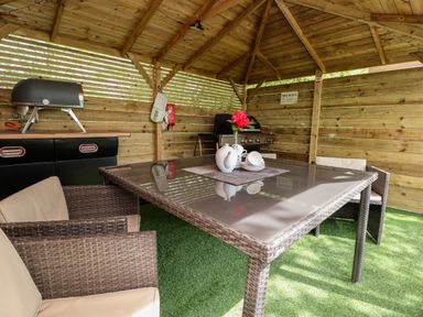 An outdoor wooden gazebo with a glass table and wicker chairs with grills and barbecue equipment at Holmside Audley Brow near Market Drayton