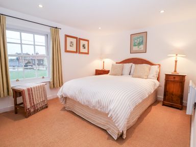 A bedroom with a double bed between two wooden nightstands each with a lamp and a window with curtains at Beta Cottage in Walberswick