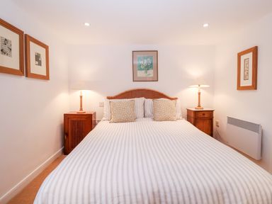 A bedroom with a double bed two bedside tables lamps and framed pictures on the walls at Beta Cottage in Walberswick