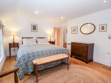 A bedroom with a bed a bench two bedside tables lamps a chest of drawers and a wall mirror at Beta Cottage in Walberswick