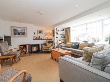 A living room with sofas chairs a coffee table a fireplace and a large window at Beta Cottage in Walberswick