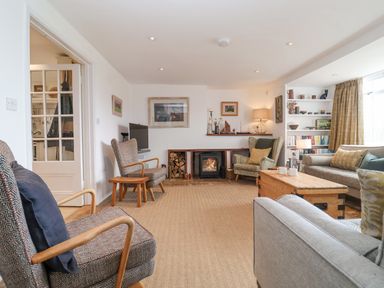 A living room with armchairs a sofa a wooden coffee table a fireplace and shelves at Beta Cottage in Walberswick