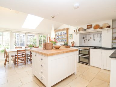 A kitchen with a large island wooden dining table and chairs skylight and stove at Beta Cottage in Walberswick
