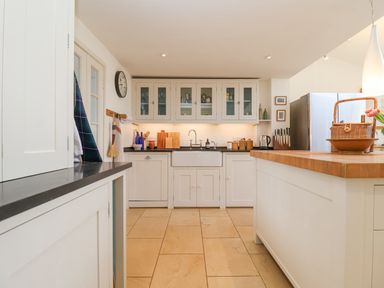 A kitchen with white cabinets a farmhouse sink wooden countertops and a refrigerator at Beta Cottage in Walberswick