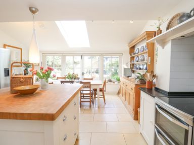 A kitchen with wooden island countertop dining table wooden chairs and cabinet with plates at Beta Cottage in Walberswick