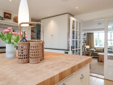 A kitchen with a wooden island countertop a wicker wine bottle holder and pink tulips on the counter at Beta Cottage in Walberswick