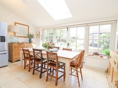 A dining room with a wooden table and six chairs next to large windows and a glass door at Beta Cottage in Walberswick