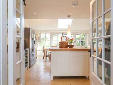 A kitchen with an island countertop a basket and flowers on the island a refrigerator and dining table with chairs at Beta Cottage in Walberswick