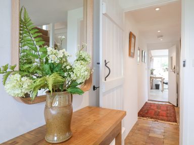 A hallway with a wooden table holding a vase of flowers and a mirror above at Beta Cottage in Walberswick