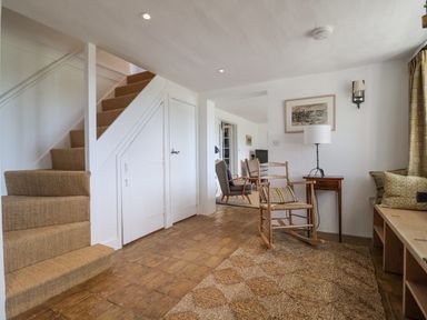 A room with carpeted stairs a rocking chair a small desk lamp and chairs at Beta Cottage in Walberswick