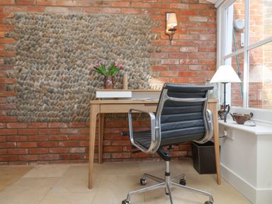 A workspace with a wooden desk and a black office chair near a window at Beta Cottage in Walberswick