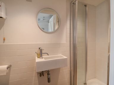 A bathroom with a wall-mounted sink mirror paper holder and shower at Beta Cottage in Walberswick