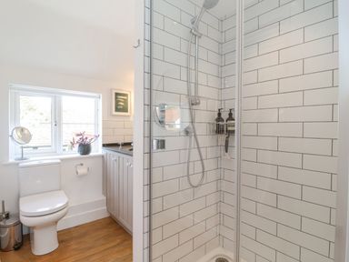 A bathroom with a shower cabin, toilet, window, and a cabinet with a sink at Beta Cottage in Walberswick