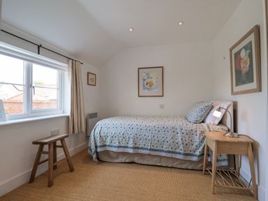 A bedroom with a single bed a wooden stool a bedside table and framed pictures on the walls at Beta Cottage in Walberswick