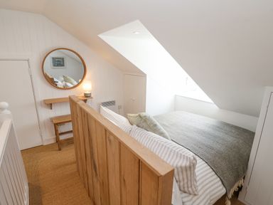 A bedroom with a wooden bed frame a striped bedspread a small wooden desk with a lamp and a round mirror on the wall at Beta Cottage in Walberswick