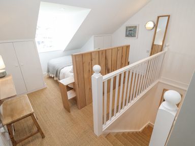 A bedroom with a bed behind a wooden headboard a wooden stool and a mirror near the staircase at Beta Cottage in Walberswick