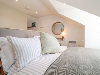 A bedroom with a bed with striped pillows a green pillow grey blanket a round wall mirror and a lamp on a small wooden shelf at Beta Cottage in Walberswick