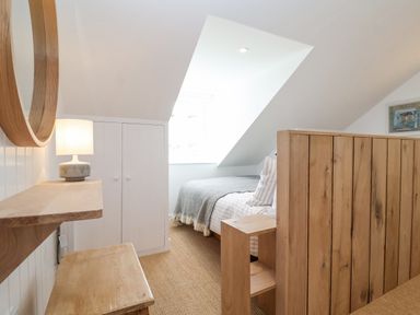 A bedroom with a wooden bed frame a bedside table a wooden bench a round wall mirror and a lamp at Beta Cottage in Walberswick