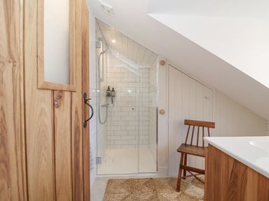 A bathroom with a glass shower enclosure wooden door wooden chair and a textured floor mat at Beta Cottage in Walberswick