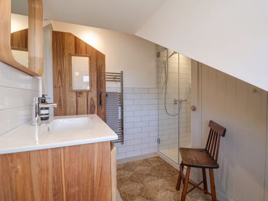 A bathroom with a wooden vanity sink cabinet a glass shower enclosure a wooden chair and a wall-mounted towel rack at Beta Cottage in Walberswick