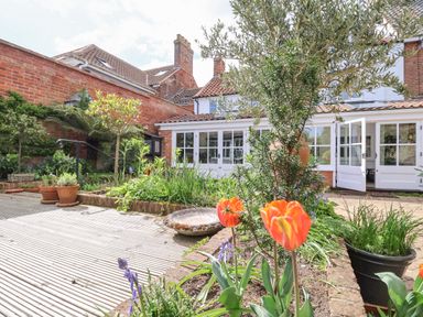 A garden with flowers and plants outside a house with white framed glass doors at Beta Cottage in Walberswick
