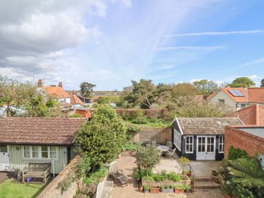 A backyard with patio furniture and garden sheds surrounded by trees and houses at Beta Cottage in Walberswick