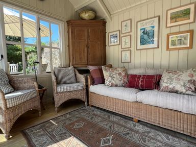 A sitting area with wicker furniture cushions and framed pictures on the wall at Beta Cottage in Walberswick