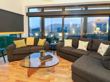 A living room with gray sofas and a glass coffee table in front of large windows at 2 Strathtay Lodges in Aberfeldy