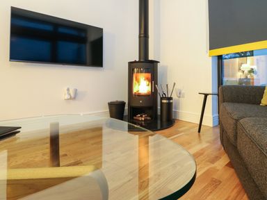 A living room with a wall-mounted TV wood burning stove gray sofa and glass coffee table at 2 Strathtay Lodges in Aberfeldy