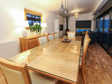 A dining room with a glass top wooden table and chairs a sideboard with lamps and a plant a living area with a sofa and a wood stove at 2 Strathtay Lodges in Aberfeldy