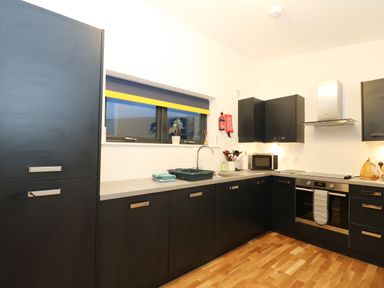 A kitchen with black cabinets a window with a yellow and blue blind and a wooden floor at 2 Strathtay Lodges in Aberfeldy