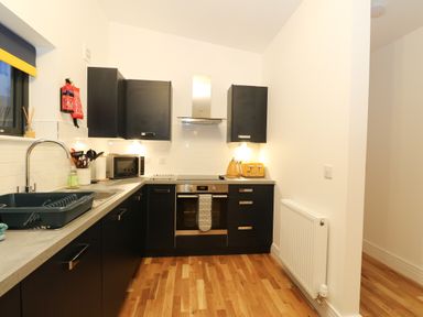 A kitchen with black cabinets a stainless steel oven microwave kettle toaster and wooden floor at 2 Strathtay Lodges in Aberfeldy