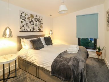 A bedroom with a double bed gray pillows and blanket side table pendant lights and a window with blue blind at 2 Strathtay Lodges Aberfeldy