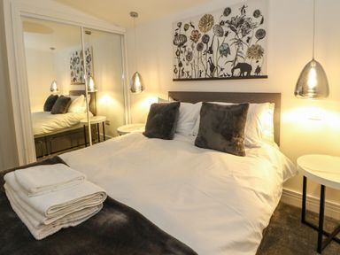 A bedroom with a double bed white bedding gray pillows bedside tables pendant lights and mirrored wardrobe at 2 Strathtay Lodges Aberfeldy