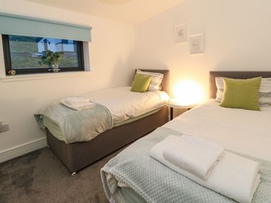 A bedroom with two single beds with green pillows and folded towels at 2 Strathtay Lodges in Aberfeldy