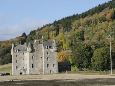A stone castle surrounded by trees and a field at 2 Strathtay Lodges in Aberfeldy