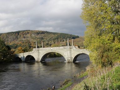A stone bridge over a river with trees and hills in the background at 2 Strathtay Lodges in Aberfeldy